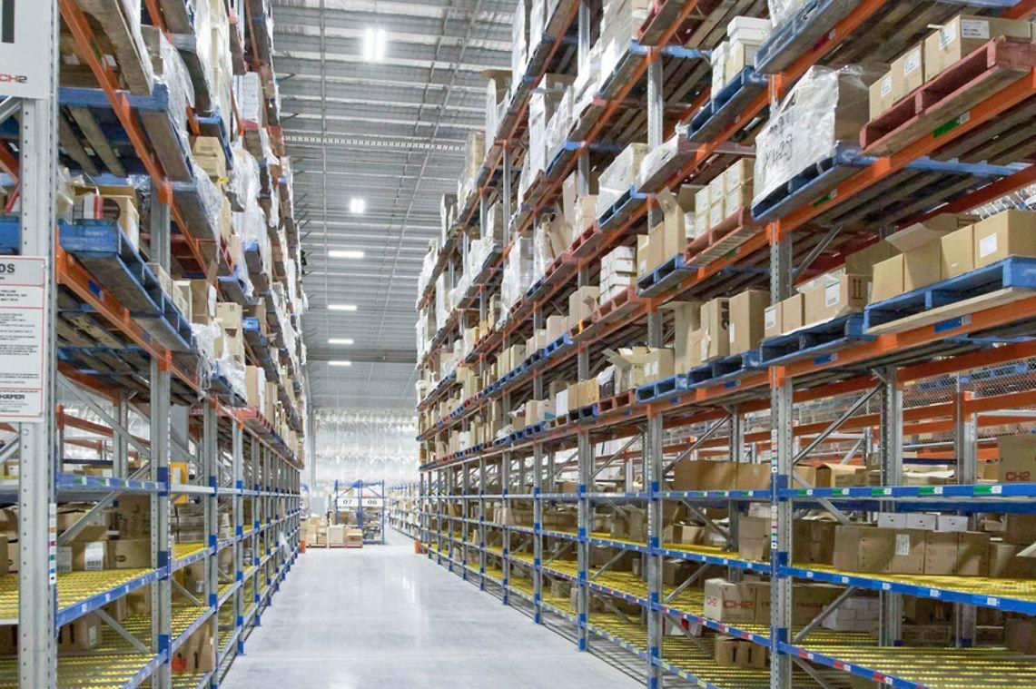 Warehouse aisle with tall storage racks, organised inventory and a worker, illustrating stock management and e-commerce fulfilment.